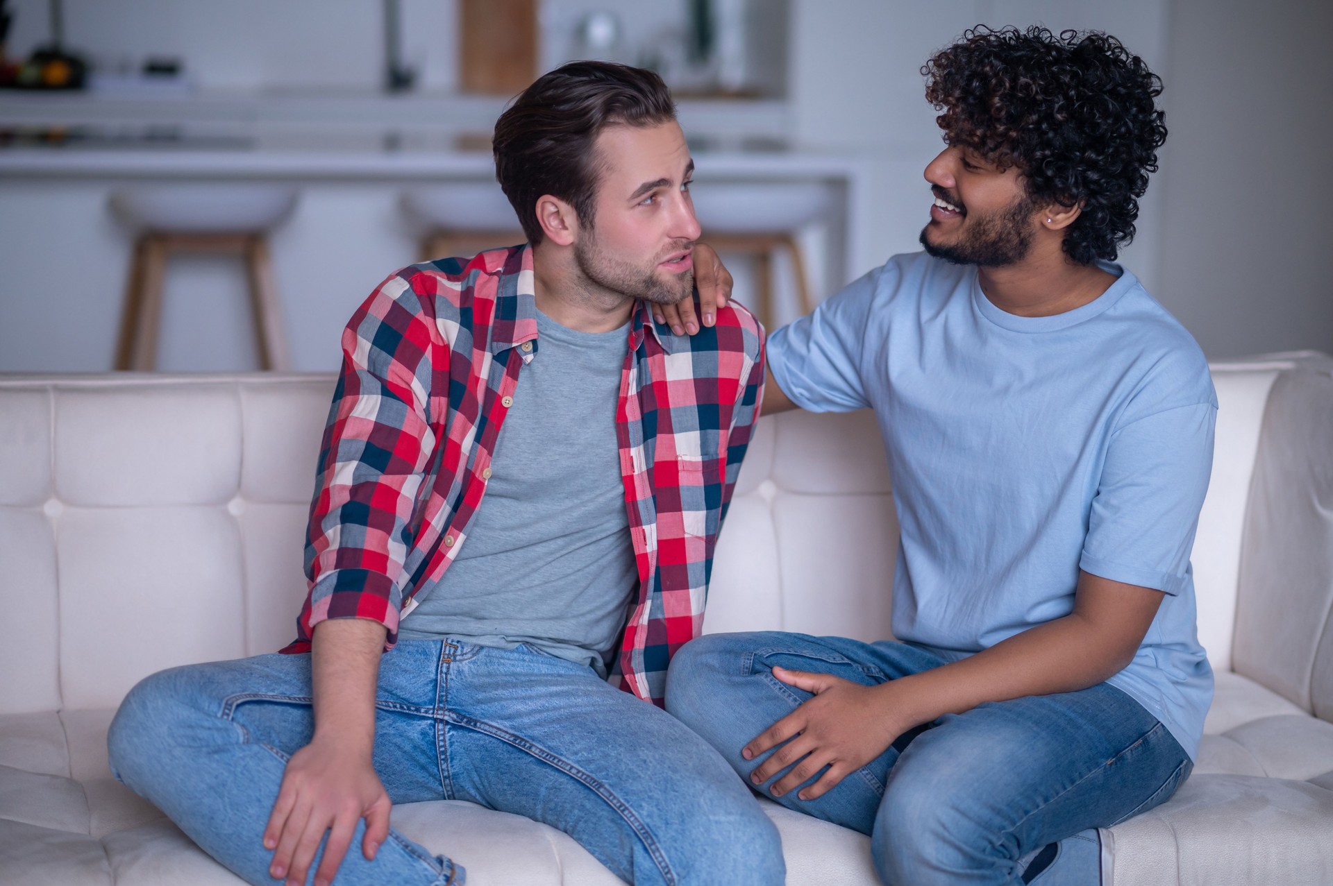 Biracial gay couple having a conversation on the sofa